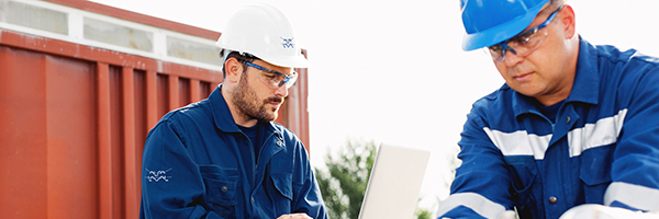 Two engineers wearing white and blue hard hats working outside